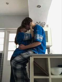 a man and woman sitting on top of a kitchen counter kissing each other's foreheads