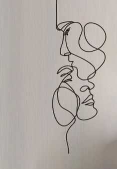 a drawing of a woman's face hanging from a string on a wall with a vase in the background