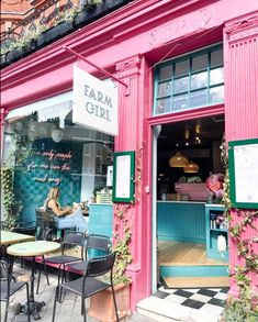 a pink and blue store front with people sitting at tables in the doorway, outside