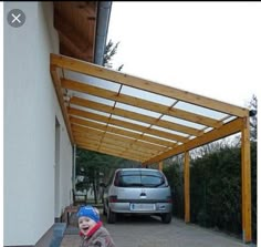 a small child standing in front of a car under a carportusure on the side of a building