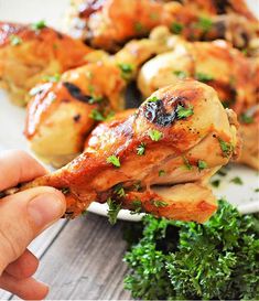 someone is holding up a piece of chicken with parsley on it and some other food in the background