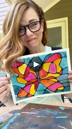 a woman holding up a colorful butterfly art piece