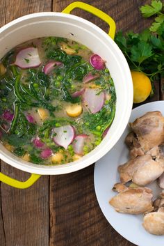 a white bowl filled with soup next to sliced lemons and parsley on a wooden table