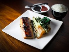 a white plate topped with fish and vegetables next to rice on a wooden counter top