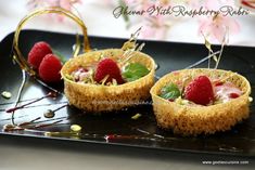 three small desserts with raspberries on a black plate