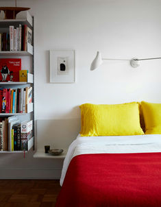 a bed with yellow and red pillows in a bedroom next to a bookshelf