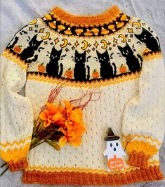 a knitted sweater with an orange flower and a small pumpkin on the bottom, sitting next to it