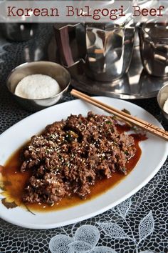 a white plate topped with meat covered in gravy next to two silver bowls