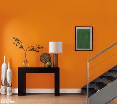 an orange room with two vases and a lamp on a table next to the stairs