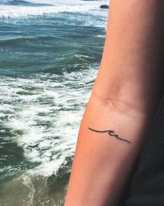 a woman's arm with a small tattoo on it, near the ocean waves