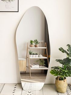 an oval mirror sitting on top of a white floor next to a potted plant