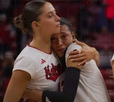 two female volleyball players hugging each other on the court