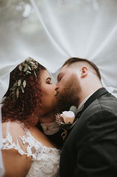 a bride and groom kissing in front of a white backdrop