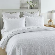 a bed with white comforters and pillows in a bedroom