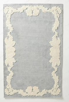 a gray and white rug with an ornate border on the bottom, in front of a wall