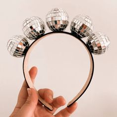 a hand holding a mirror with disco balls on it's headband and pointing at the mirror