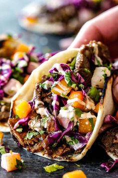 a hand holding a taco filled with meat and veggies next to other food