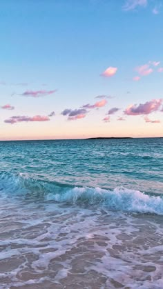 the ocean waves come in to shore as the sun is setting on the horizon and there are pink clouds