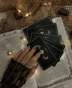 a woman's hand holding four cards in front of an open book with lights on it