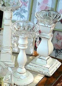 three white candlesticks sitting on top of a table next to other glass vases