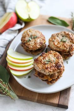 three crab cakes on a white plate with apples and sage leaves next to the plate