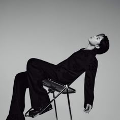 a man sitting on top of a chair with his feet up in the air while wearing black pants