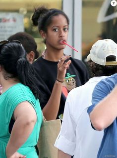 a woman with a straw in her mouth standing next to other people and looking at the camera