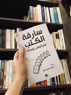 a person holding up a book in front of a bookshelf filled with books