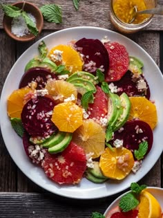 a white plate topped with fruit salad next to another plate filled with oranges, avocado and other fruits