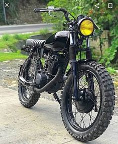 a black motorcycle parked on the side of a road next to some bushes and trees