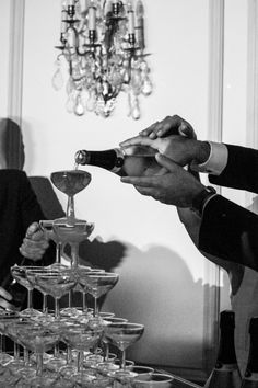 two men in suits are pouring champagne into wine glasses on a table with other people