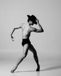 a shirtless man wearing a cowboy hat and black swim trunks is dancing in the studio