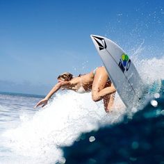 a woman riding a surfboard on top of a wave in the ocean with blue sky