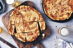 two pizzas sitting on top of a wooden cutting board next to glasses of beer