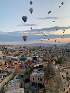 many hot air balloons are flying in the sky above some buildings and trees, with mountains in the background