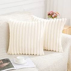 two white pillows sitting on top of a couch next to a cup and saucer