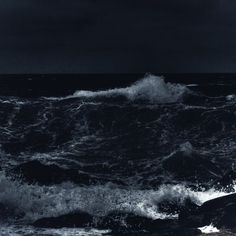 a black and white photo of waves crashing on the rocks in the ocean at night