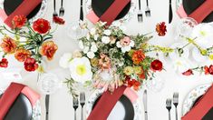 the table is set with black plates, silverware and red napkins that have flowers on them