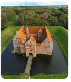 an aerial view of a castle in the middle of a field with water and trees