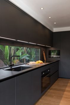 a modern kitchen with black cabinets and wood flooring is pictured in this image, there are fruit on the counter