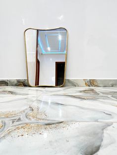 a bathroom mirror sitting on top of a marble counter next to a wall mounted toilet paper dispenser