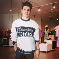 a young man standing in front of a store display wearing a white sweater with black lettering on it