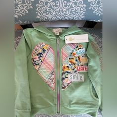 a green jacket with patchwork heart patches on the front and back, hanging from a hanger