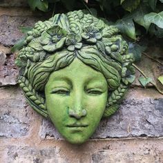 a green face with flowers on it is mounted to the side of a brick wall