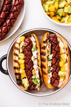 two hot dogs on buns with toppings in a pan, ready to be eaten