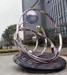 a large metal sculpture sitting on top of a sidewalk next to a tall glass building