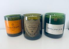 three candles sitting next to each other on a white counter top with wine bottles in the background