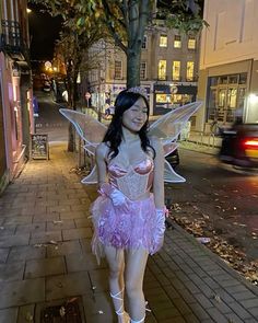 a woman dressed as a fairy standing on the sidewalk