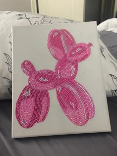 a canvas with pink beads on it sitting on top of a bed next to pillows