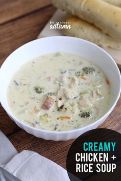 a bowl of creamy chicken and rice soup next to a baguette on a cutting board